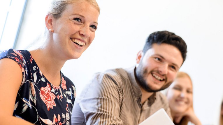 Zwei Studentinnen und ein Student lachend mit Unterlagen