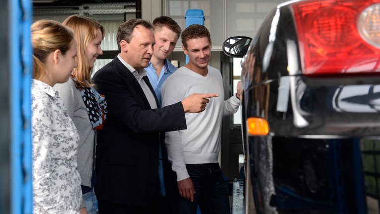 Lehrender und Studierende neben einem Fahrzeug