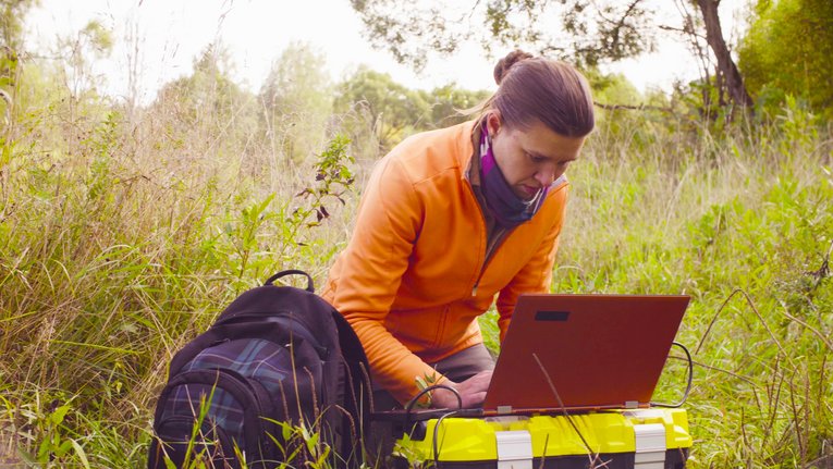 Wissenschaftlerin arbeitet im Wald am Laptop